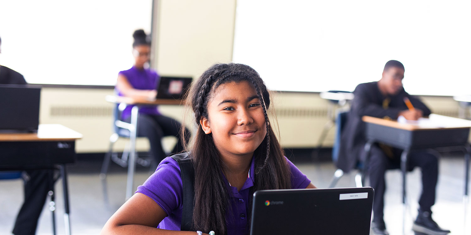 Smiling middle school student sitting at desk in a classroom.
